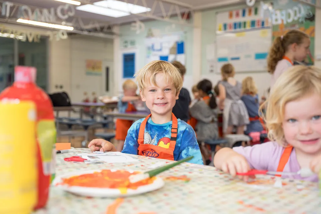 Boy smiling whilst sat at an arts & crafts table